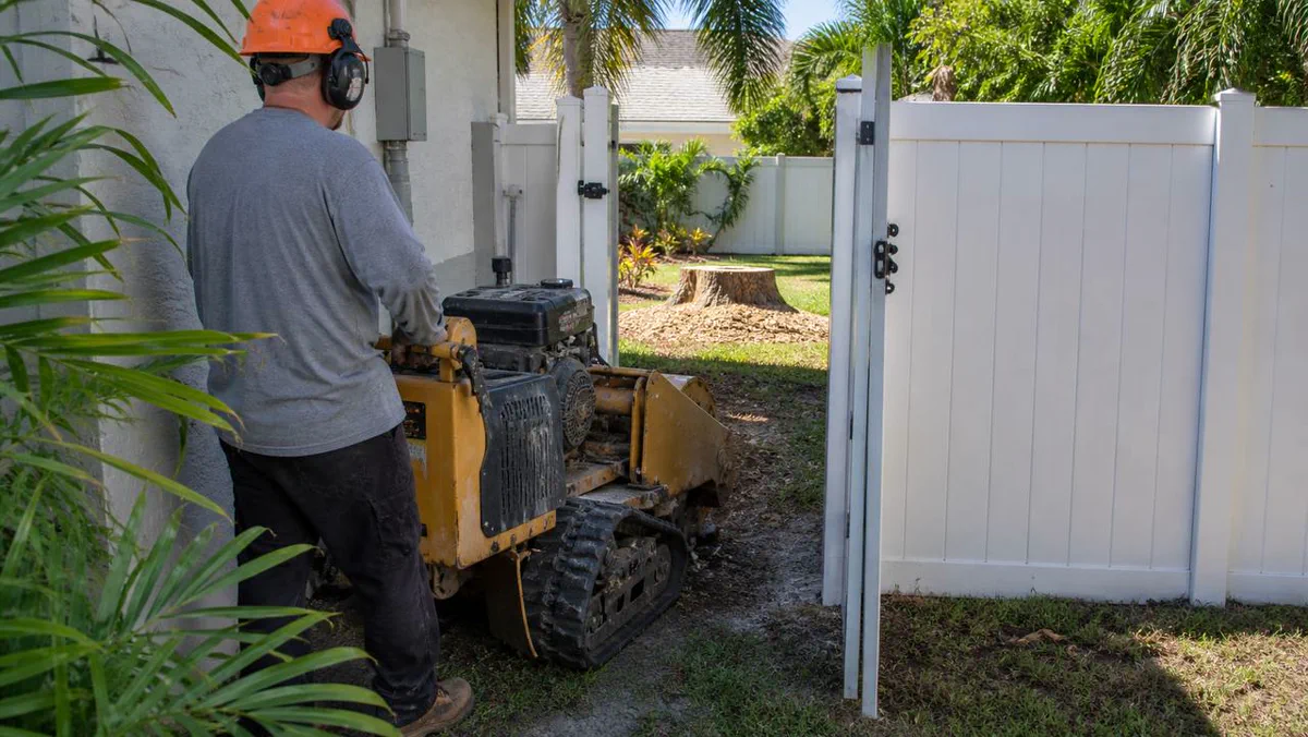 Compact stump grinder accessing a fenced Melbourne FL backyard through a side gate